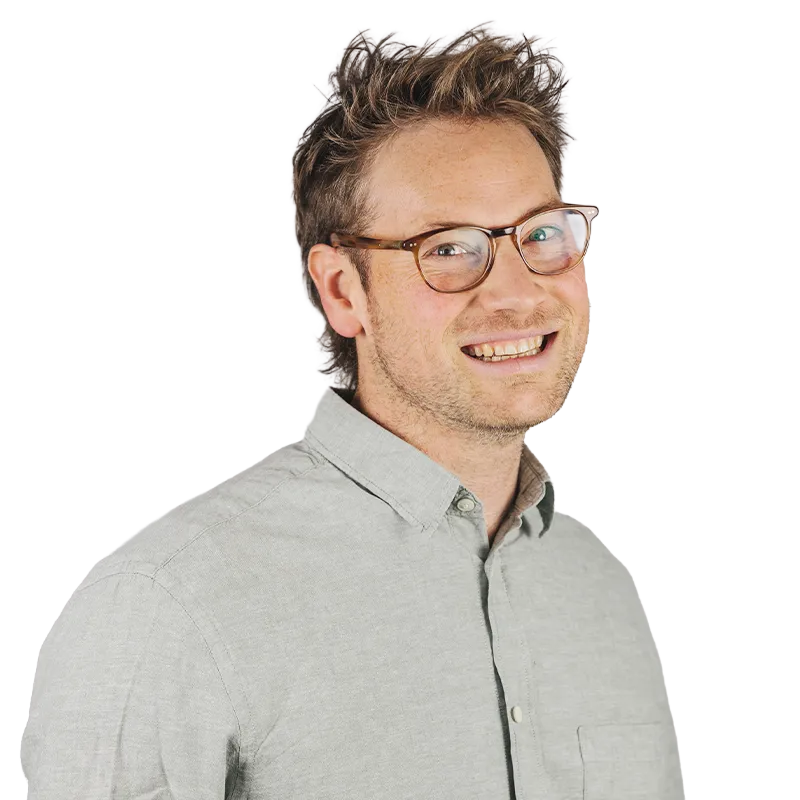 Mann mit Brille und lächelndem Gesicht, trägt ein hellgraues Hemd.