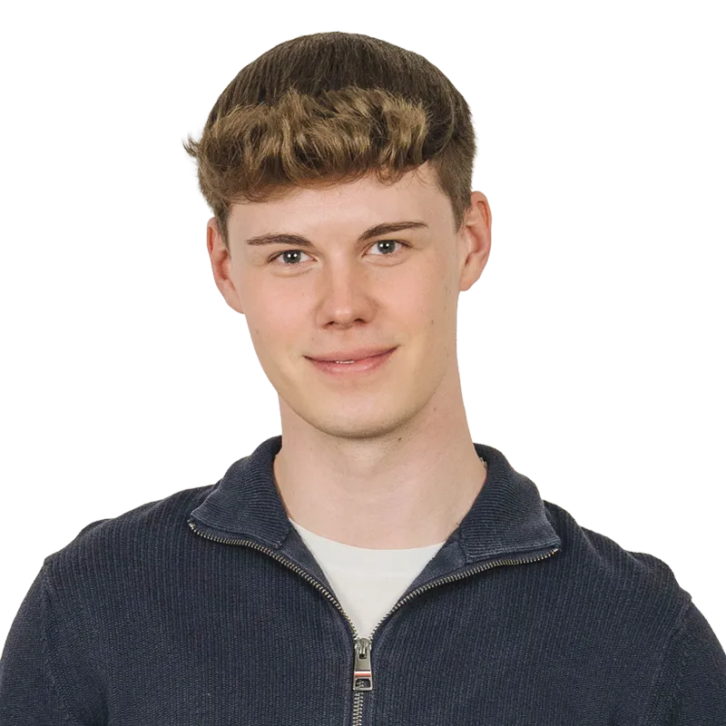Junger Mann mit kurzem, welligem Haar und einem blauen Pullover, der in die Kamera lächelt.